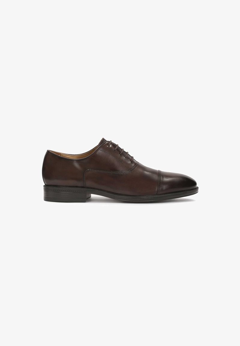 Chaussure habillée en cuir marron avec une finition lisse, bout rond, système de laçage et un petit talon en caoutchouc noir. Comprend des détails cousus sur les côtés.