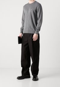 Maglione grigio lavorato a maglia con collo rotondo, abbinato a pantaloni neri a gamba larga. Scarpe nere in pelle completano il look, tenute con una pochette nera.