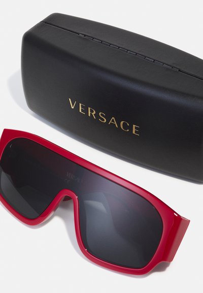 Ochelari de soare roșii supradimensionați cu o ramă groasă din plastic și lentile întunecate, însoțiți de o husă neagră cu inscripția aurie "VERSACE".