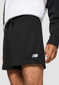 Shorts de sport en maille noire avec taille élastique, cordon de serrage et logo blanc. Tissu léger avec surface texturée.