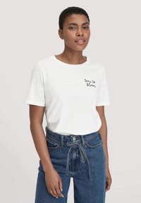 Witte katoenen T-shirt met korte mouwen en de tekst "tijd om te bloeien" in het zwart. Gecombineerd met high-waisted denim jeans.