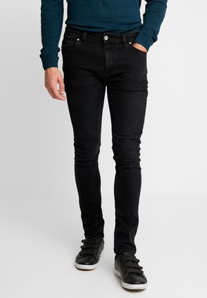 Jeans de mezclilla negra con un diseño ajustado, estilo de cinco bolsillos y una textura suave, combinados con zapatillas negras con múltiples correas.