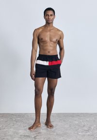 Μαύρα μαγιό σορτς με οριζόντιες ρίγες σε κόκκινο, λευκό και ανοιχτό ροζ. Μέση με κορδόνι, ελαφρύ ύφασμα και άνετη εφαρμογή.