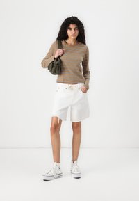 Stripet langermet topp i brun og beige, kombinert med hvite denimshorts med frynser. Hvite høyhælte joggesko og grønn veske.