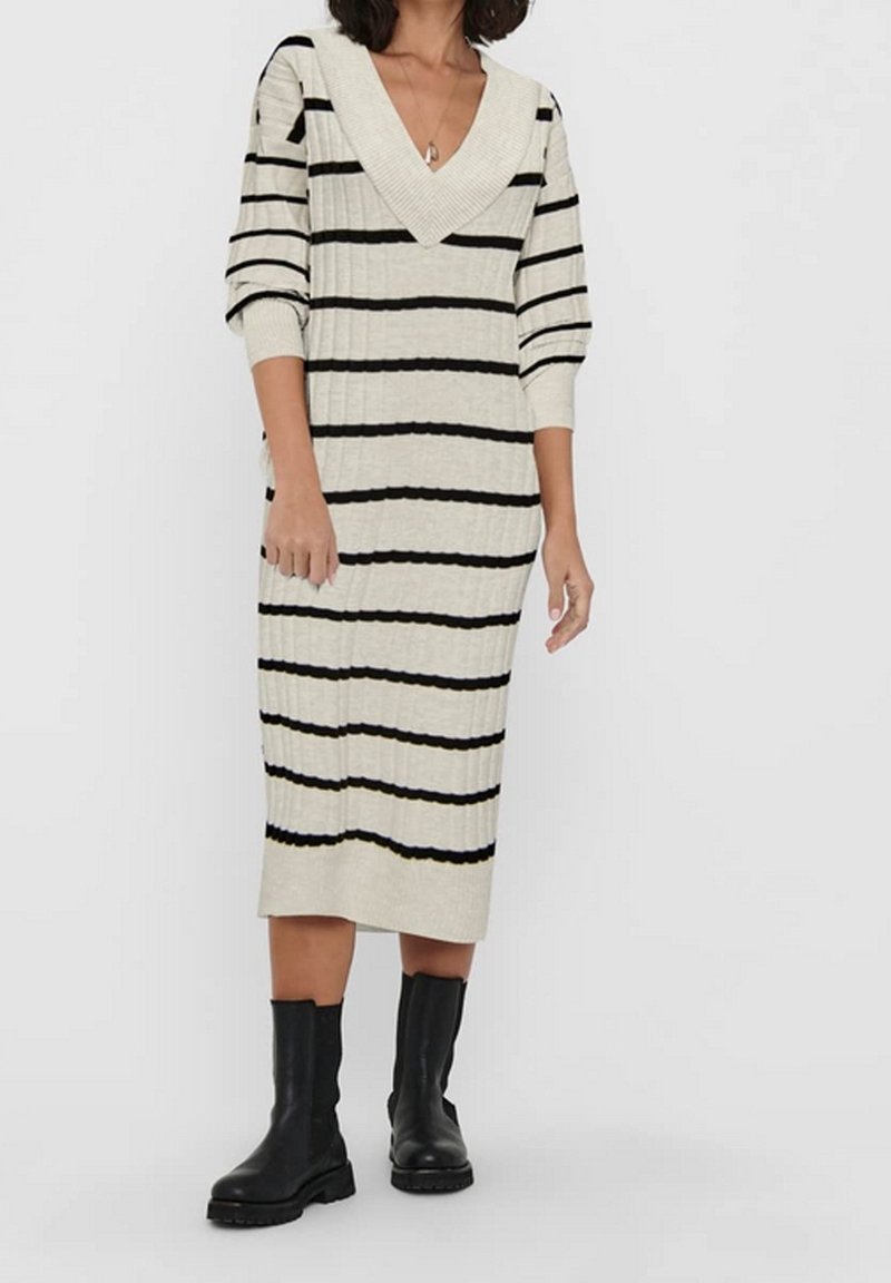 Robe en tricot de couleur crème avec des rayures horizontales noires, dotée d'un décolleté en V profond et de manches trois-quarts, associée à des bottines noires.