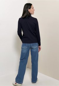 Granatowa bluzka z długim rękawem w połączeniu z jasnoniebieskimi prostymi dżinsami. Bluzka ma wysoki kołnierz, a dżinsy mają klasyczny fason z pięcioma kieszeniami.