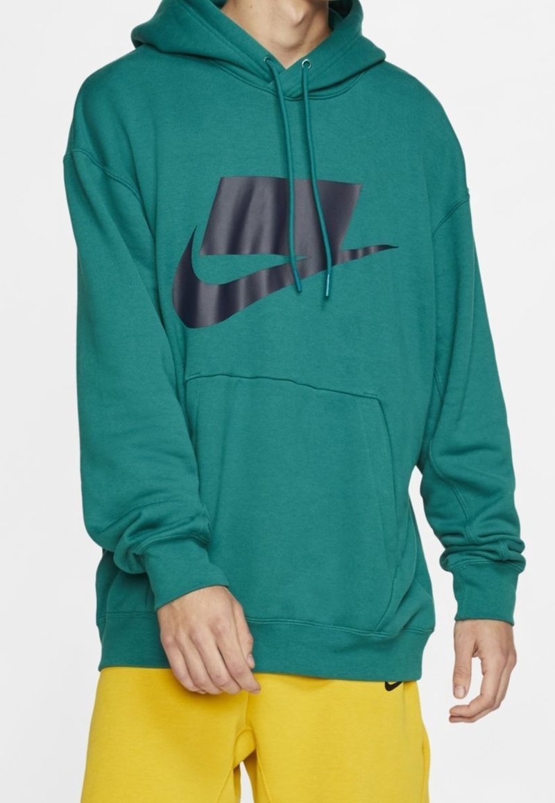 Teal huppari, joka on valmistettu puuvillasekoitteesta, jossa on suuri musta Nike-logo rinnan kohdalla, kengurutasku ja säädettävä nyörihuppu.