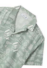 Camicia a maniche corte in tessuto verde chiaro con motivi geometrici bianchi. Presenta un colletto classico e una chiusura con bottoni, taglia XL.
