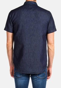 Camisa de denim oscuro de manga corta con cuello button-down, textura sutil y dobladillo curvado, combinada con jeans ajustados.