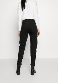 Czarne jeansy z wysokim stanem i prostą nogawką, z dwiema tylnymi kieszeniami i gładką fakturą denimu, w połączeniu z białą bluzką z długim rękawem.