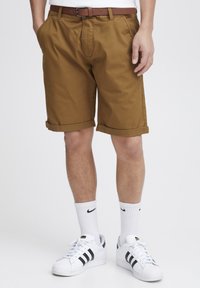 Khaki shorts with rolled cuffs, side pockets, and a front pleat, paired with white sneakers and athletic socks featuring a black logo.