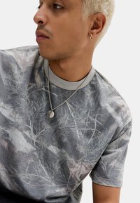 Grå kortærmet T-shirt med et slidtegn botanisk print, kombineret med en rund halsudskæring og lagdelt med en sølvkæde.