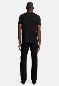 T-shirt in cotone nero con maniche corte, design semplice e scollatura a girocollo, abbinata a jeans neri a gamba dritta e scarpe nere eleganti.