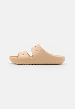 Beige slip-on sandal made from flexible material, featuring two wide cutouts, ventilation holes, and a textured sole for grip.