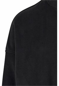 Svart fleece-stoff med en glatt tekstur, høy hals og senket skuldersømmer. Minimalistisk design uten synlige detaljer.