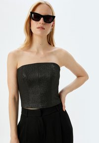 Sort tube top med en tekstureret overflade, parret med højtaljede sorte bukser. Modellen bærer sorte katteøje solbriller.