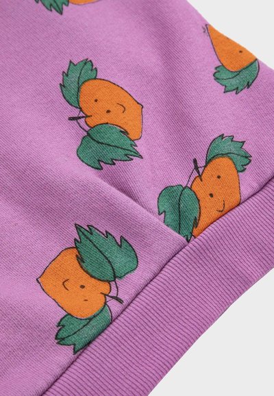 Fialová látka s ilustráciami usmievavých oranžových ovocí a zelenými listami vytlačenými pozdĺž pruhovaného lemu manžety.