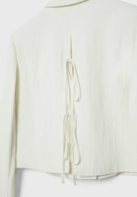Dos d'une veste blanche à manches longues avec un col et deux cordons noués suspendus à une fente verticale au centre.