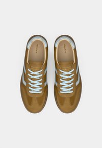 Καφέ σουέντ αθλητικά παπούτσια με ανοιχτό μπλε λεπτομέρειες. Διαθέτουν επίπεδα κορδόνια, στρογγυλεμένη μύτη, δίχρωμο σχέδιο και λογότυπο στη γλώσσα.