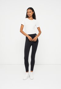 Vit kortärmad topp som kombineras med högmidjade svarta leggings. Sneakers är vita. Slät textur med en åtsittande design, utan mönster.