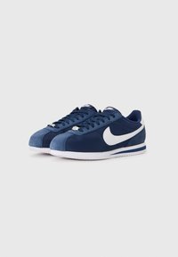 Ténis azul marinho com parte superior em camurça e tecido, logótipo swoosh branco, atacadores planos e sola de borracha texturizada. Design retro clássico.