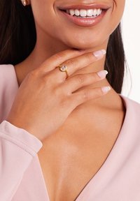 Gold ring featuring a round purple gemstone, set in textured metal. Model's hand is elegantly positioned near her face, showcasing the ring.