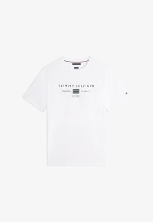 Bílé tričko s krátkým rukávem s nápisem „Tommy Hilfiger American Classics Est. 1985“ a grafikou zeleného tenisového kurtu na hrudi.