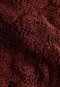 Gros plan sur un textile brun foncé avec un motif complexe de boucles et de travail ajouré, montrant une texture douce et des détails en relief.