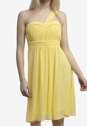 Kvinde iført en gul, ærmeløs kjole med en enkelt strop, der krydser diagonalt over den ene skulder og med plisseret bodice.
