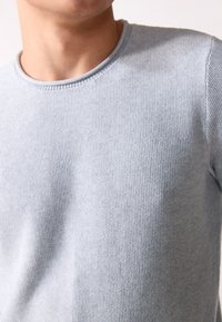 Pull en tricot bleu clair avec un col rond et un motif texturé. Le tissu semble doux et extensible.