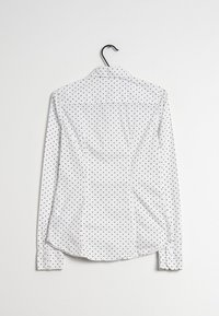 Vit långärmad skjorta med svarta prickar, med klassisk krage och knäppärmar, tillverkad av ett slätt tyg.