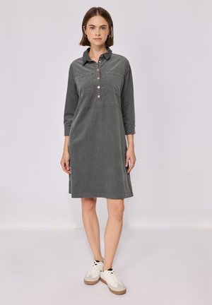 Grijze corduroy jurk met een kraag, knoopsluiting en driekwart mouwen. Gestyled met witte sneakers voor een casual look.