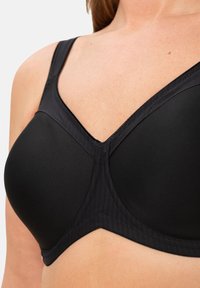 Musta liivi, jossa on sileä kangas, V-pääntie, säädettävät olkahihnat ja vahvistettu ommel tukea varten. Ei näkyviä kuvioita tai kiinnikkeitä.