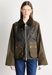 Waxed cotton jacket in dark olive and black, featuring a corduroy collar, gold hardware, two front pockets, and a zip closure.