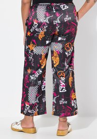 Pantaloni neri larghi con una vivace stampa grafica caratterizzata da accenti rosa, arancioni e bianchi, tra cui tigri e motivi a scacchi.