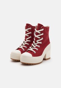 Sneaker alte rosse in tessuto textured, con punta in gomma bianca e tacco spesso beige. Presentano lacci bianchi e un logo decorativo.