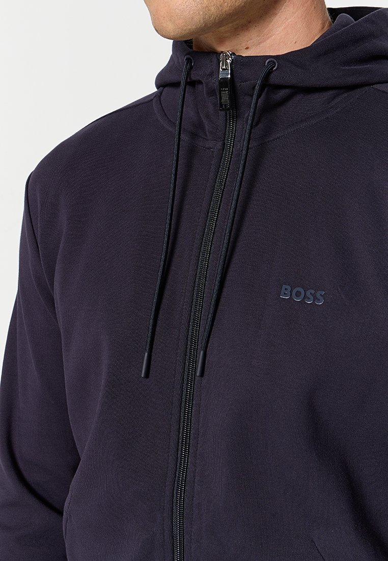 Uomo che indossa un cappuccio zip-up di un blu scuro con coulisse e un piccolo logo "BOSS" sul petto sinistro.