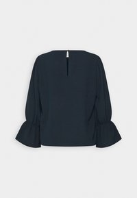 Blouse noire à manches longues avec fermeture boutonnière en forme de trou à l'encolure arrière et bracelets évasés aux manches sur un fond uni.