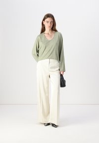 Light green long-sleeve top with a V-neck, paired with high-waisted white wide-leg pants. Model holds a small black handbag.