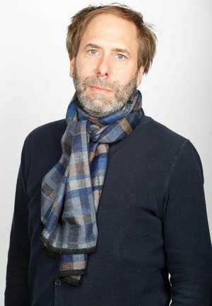 Plaid scarf in blue, gray, and brown wrapped around neck; made of soft fabric with fringed edges, worn over a dark sweater.