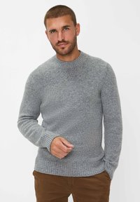 Grauer Strickpullover mit rundem Halsausschnitt, gerippten Bündchen und Saum. Der strukturierte Stoff zeigt leichte Sprenkel. Wird mit braunen Hosen getragen.