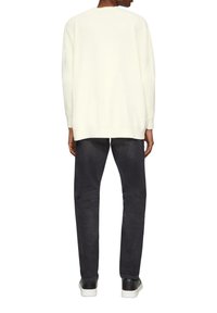 Weißer Strickpullover mit Rundhalsausschnitt, getragen über dunkelgrauen Slim-Fit-Hosen und schwarzen Sneakers mit weißen Sohlen.