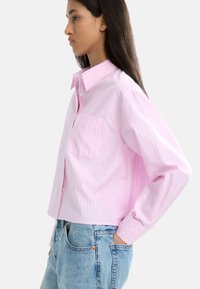 Jasnoróżowa, skrócona koszula z guzikami w białe paski, z jedną kieszonką na piersi i długimi rękawami, połączona z jasnoniebieskimi dżinsami.