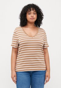 Camiseta de rayas marrones y blancas con cuello en V y mangas cortas, hecha de una tela suave, combinada con jeans azules. Logo de marca notable en el pecho.