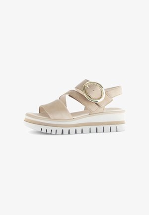 Beige platform sandals with two crossed straps, a round metallic accent, and a textured white outsole featuring a groove pattern.