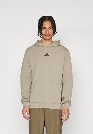 Hoodie aus hellbeigem Stoff mit langen Ärmeln, vorderer Tasche und schwarzem Logo-Detail auf der Brust. Glatte Textur und entspannte Passform.