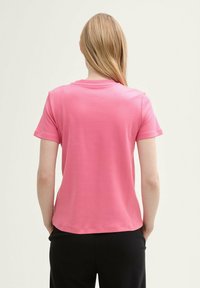 Kortärmad, bakvy av en rosa bomullströja med rund halsringning och avslappnad passform, med en mjuk textur.