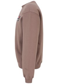 Vue latérale d'un sweat-shirt FILA mauve avec un patch logo sur la poitrine et le nom de la marque brodé sur le poignet gauche.
