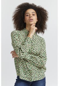Blusa a maniche lunghe con colletto di colore verde chiaro, decorata con un motivo di foglie nere e verdi sparse. Tessuto morbido e leggero, con polsini non abbottonati.