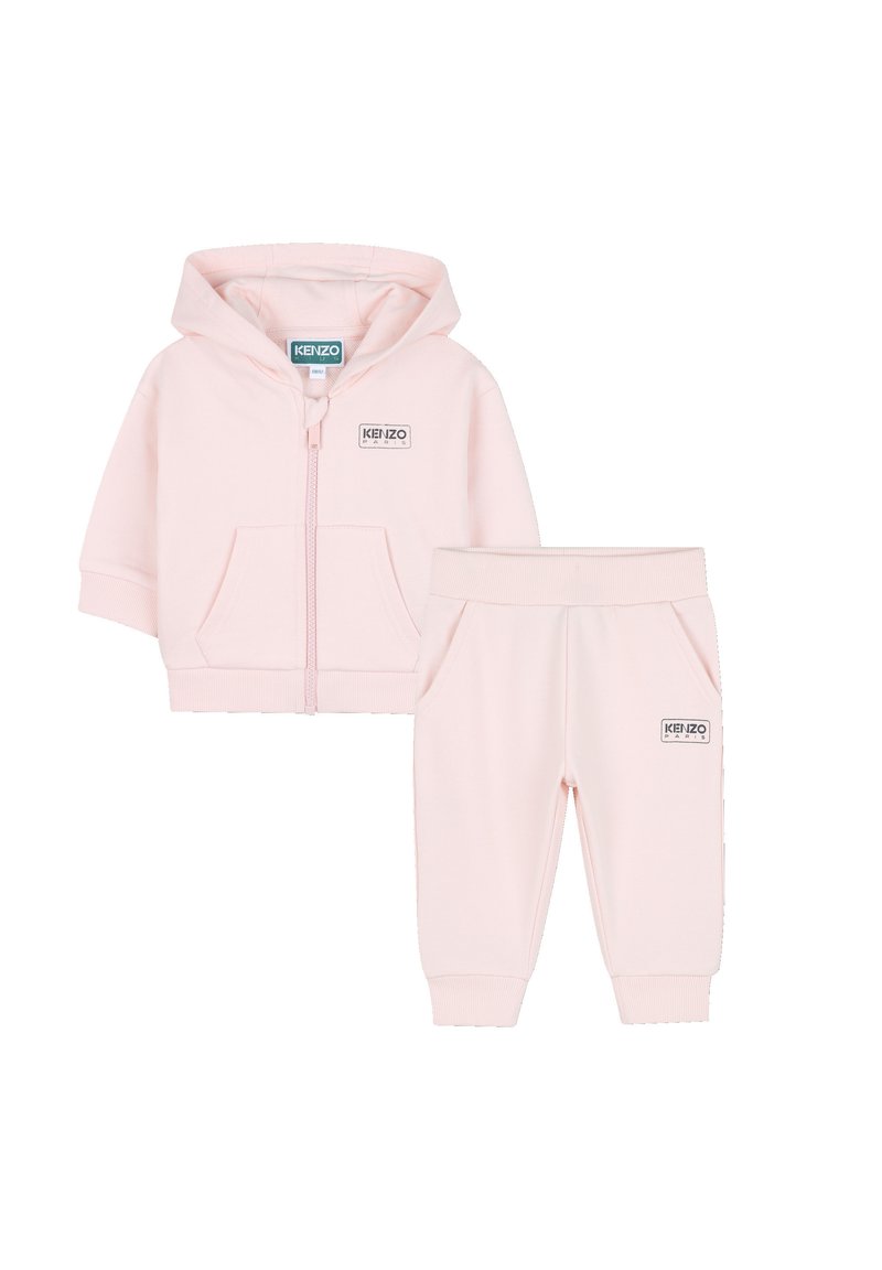 Giacca con cappuccio in rosa chiaro con zip abbinata ai pantaloni. Tessuto morbido, polsini a costine, tasche frontali e etichetta del logo su entrambi i pezzi. Design semplice.